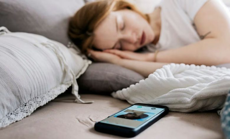 Persona despertando con dificultad y mirando el celular en la cama.